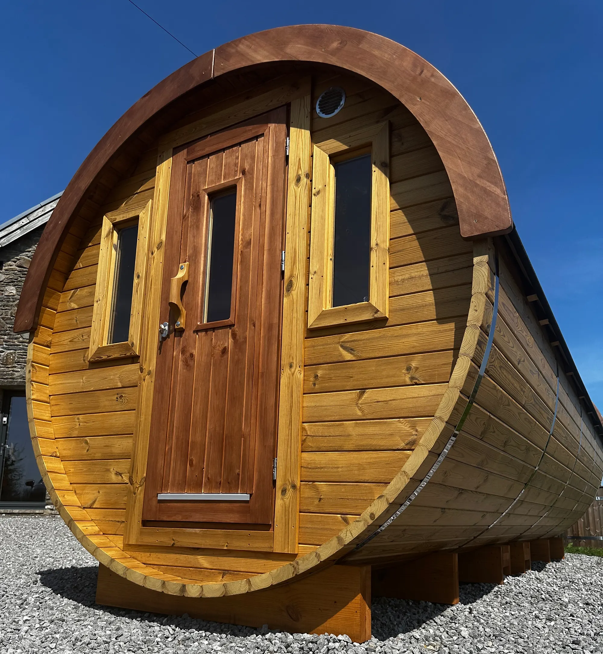 Barrel sauna exterior with cedar door under blue sky
