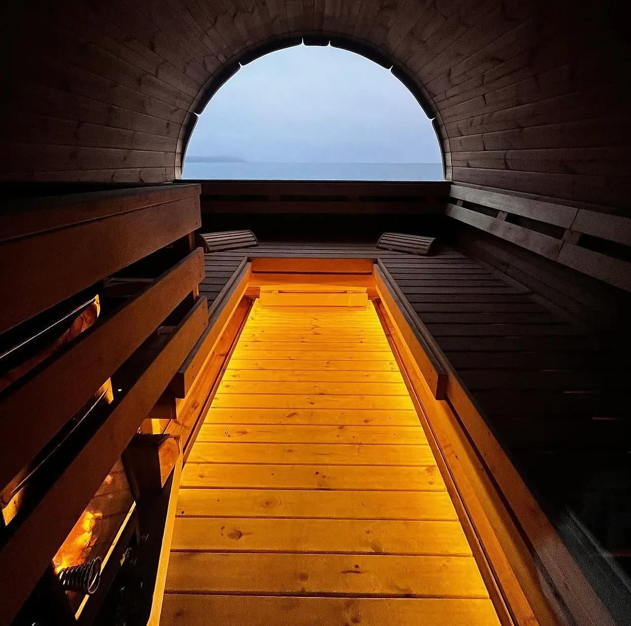 Barrel sauna interior looking out to the sea at dusk